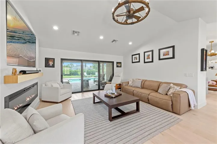 Living room featuring vaulted ceiling, a glass covered fireplace, light wood-style flooring, a chandelier, and recessed lighting