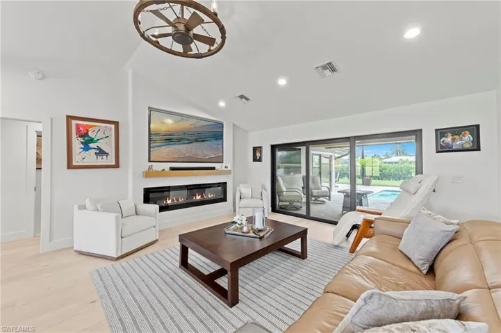 Living area featuring lofted ceiling, a glass covered fireplace, light wood-style floors, and recessed lighting