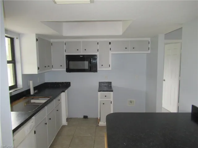 Kitchen with white dishwasher, light tile patterned floors, white cabinets, and sink