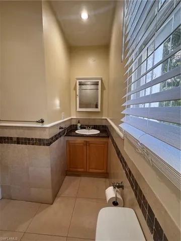 Bathroom with vanity, light tile patterned floors, wainscoting, tile walls, and recessed lighting