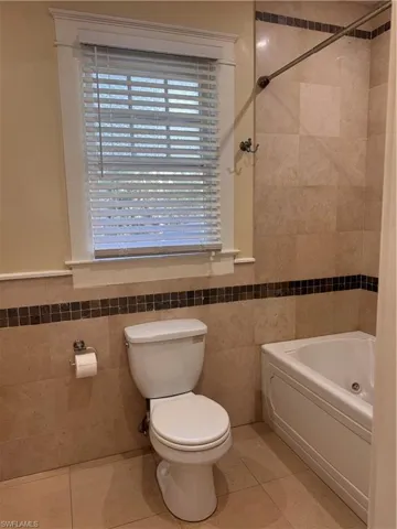 Full bath featuring tile walls, light tile patterned flooring, a combined bath / shower with jetted tub, and a wainscoted wall