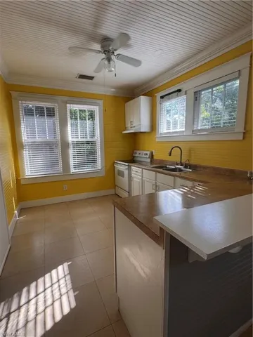 Kitchen featuring crown molding, a peninsula, white electric range oven, white cabinets, and a kitchen breakfast bar