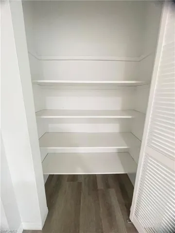 Built-in shelving unit with five white shelves, louvered bi-fold doors, and wood-finish flooring
