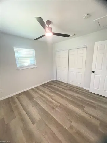 Spacious room featuring wood-finish flooring, a contemporary ceiling fan with integrated lighting, a window with blinds, and white bi-fold closet doors