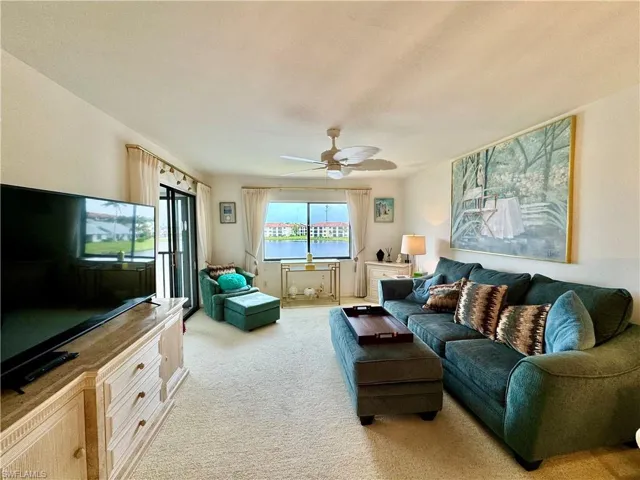 Living room with light colored carpet, a water view, and ceiling fan