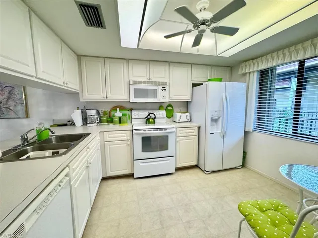 Kitchen featuring white appliances, ceiling fan, white cabinetry, and sink