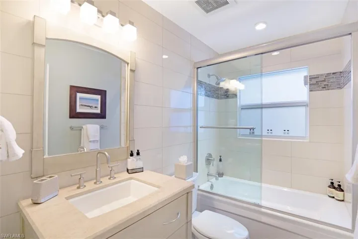 Full bathroom featuring tile walls, shower / bath combination with glass door, toilet, and vanity
