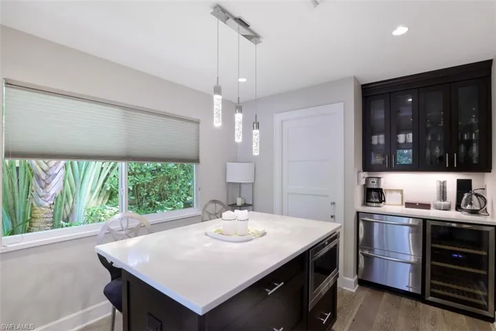 Indoor dry bar with beverage cooler, stainless steel microwave, fridge, dark wood-style flooring, and decorative light fixtures