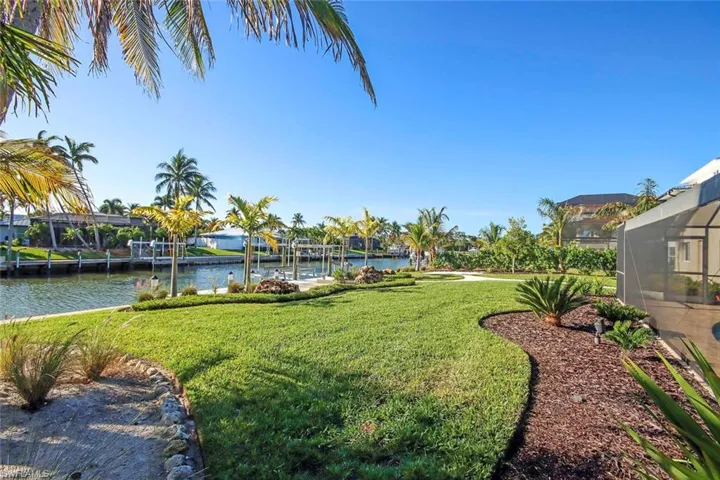 View of green lawn featuring boat lift, a water view, glass enclosure, and a boat dock