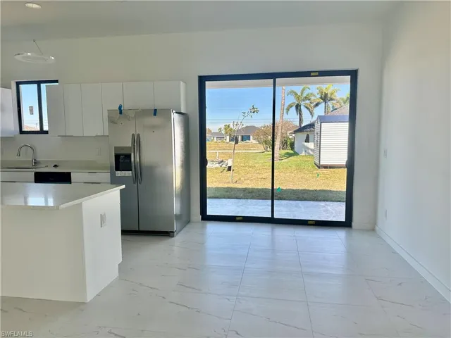 Kitchen with marble finish floor, white cabinetry, stainless steel refrigerator with ice dispenser, and light countertops