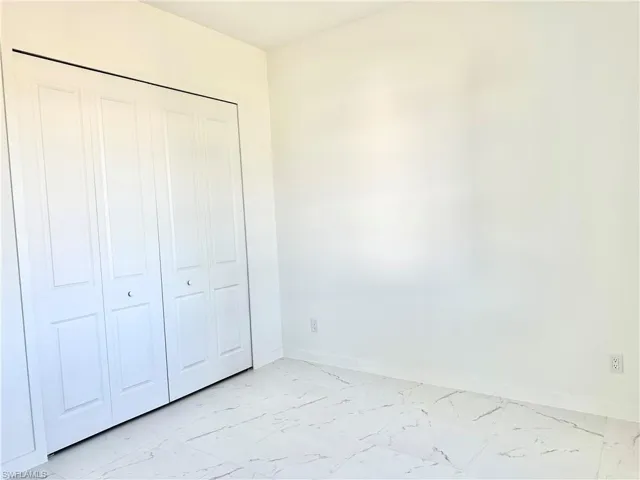 Unfurnished bedroom with marble finish floor, a closet, and baseboards