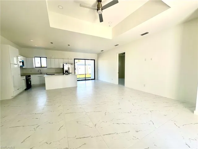 Unfurnished living room featuring marble finish floor, a tray ceiling, a sink, and visible vents