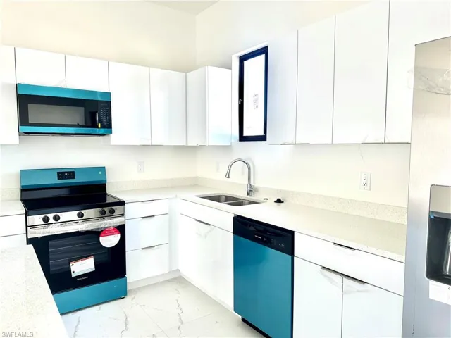 Kitchen with marble finish floor, stainless steel appliances, light countertops, white cabinets, and a sink