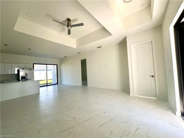 Unfurnished living room featuring a raised ceiling, ceiling fan, marble finish floor, and baseboards