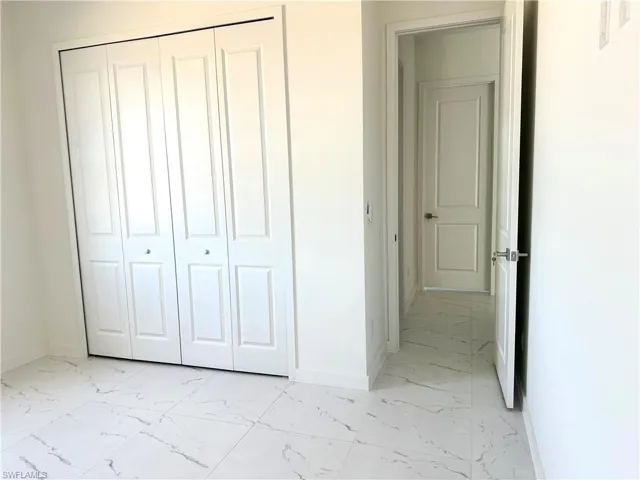 Unfurnished bedroom featuring marble finish floor, baseboards, and a closet