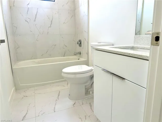 Bathroom featuring marble finish floor, shower / bath combination, vanity, and toilet