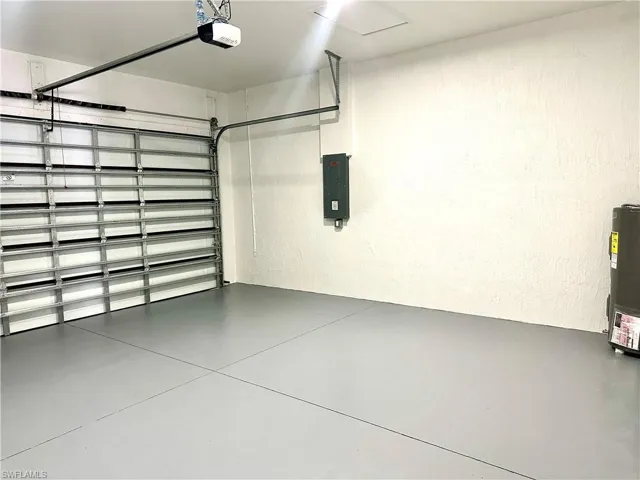 Garage with a textured wall, electric panel, a garage door opener, and electric water heater