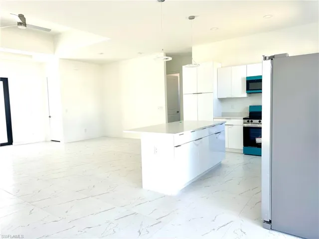 Kitchen with a kitchen island, white cabinets, marble finish floor, appliances with stainless steel finishes, and decorative light fixtures