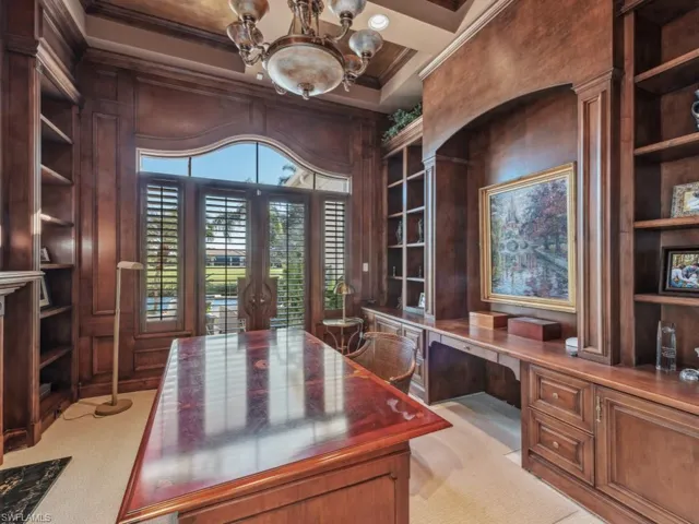 Office area featuring a notable chandelier, wood walls, light colored carpet, built in desk, and ornamental molding