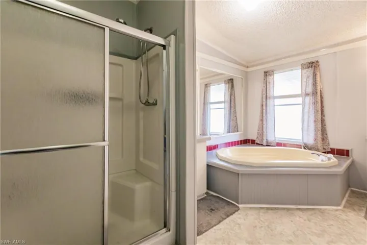 Bathroom with a textured ceiling, vaulted ceiling, and separate shower and tub
