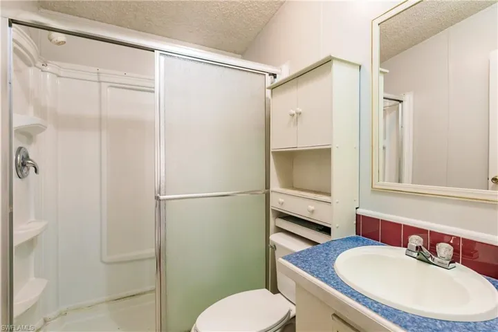 Bathroom featuring vanity, a textured ceiling, toilet, and a shower with shower door