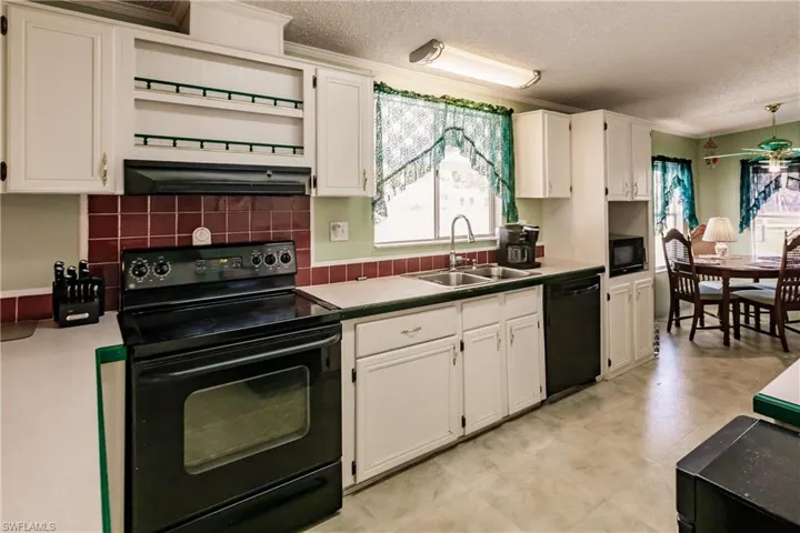 Kitchen with black appliances, sink, white cabinets, and a textured ceiling