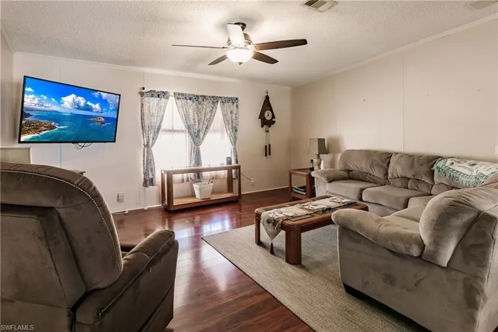 Living room featuring ceiling fan, dark hardwood / wood-style flooring, crown molding, and a textured ceiling