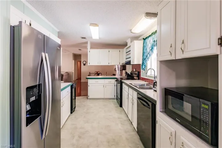 Kitchen with a textured ceiling, sink, white cabinetry, and black appliances