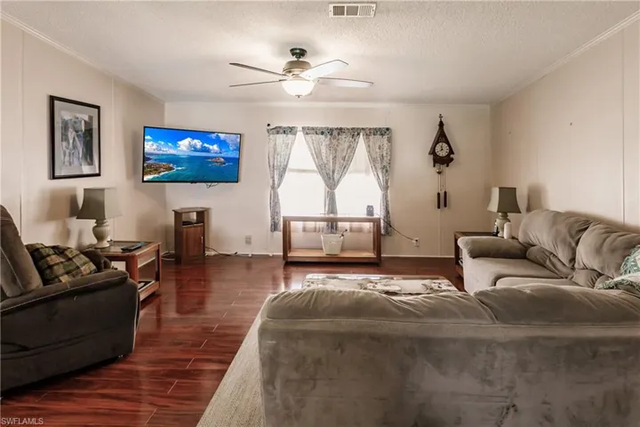 Living room featuring ceiling fan, crown molding, dark hardwood / wood-style floors, and a textured ceiling