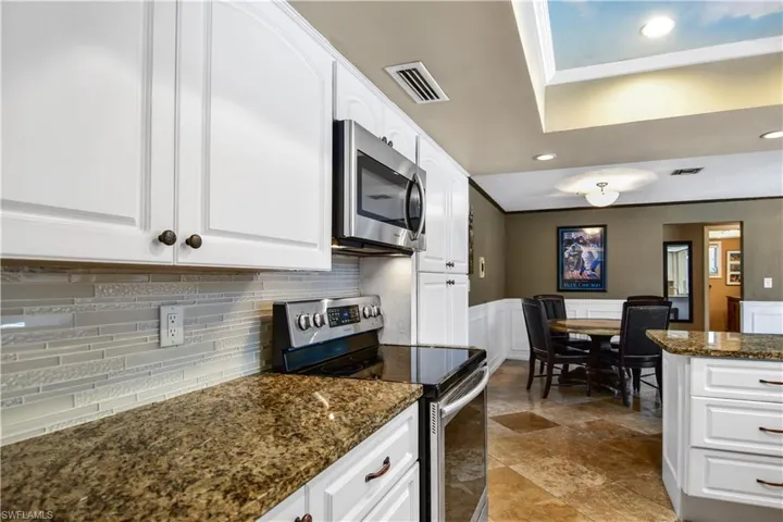 Kitchen featuring tasteful backsplash, granite countertops, white cabinets, raised ceiling and appliances with stainless steel finishes