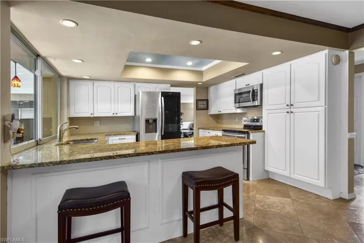 Kitchen featuring white cabinets, breakfast bar, sink overlooking the pool area, and appliances with stainless steel finishes
