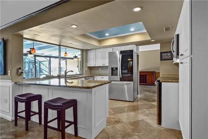 Kitchen with kitchen peninsula, stainless steel appliances, white cabinetry, and granite countertops