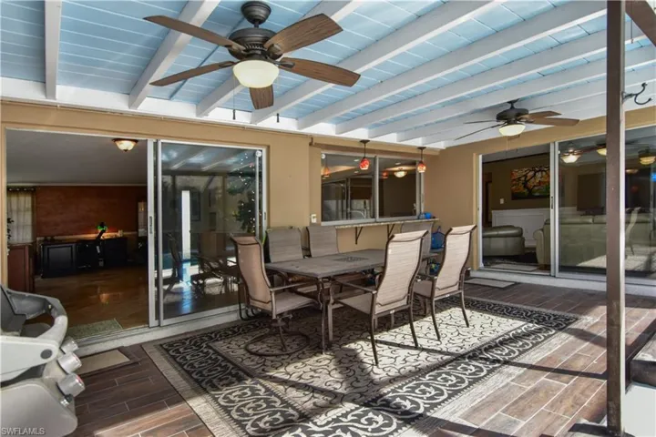 Lanai featuring plank wood-like tile, beam ceiling, sliders to both living areas, and a pass-through window to the kitchen