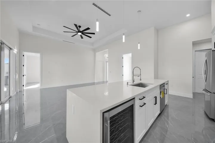 Kitchen featuring wine cooler, a tray ceiling, decorative light fixtures, stainless steel appliances, and a sink