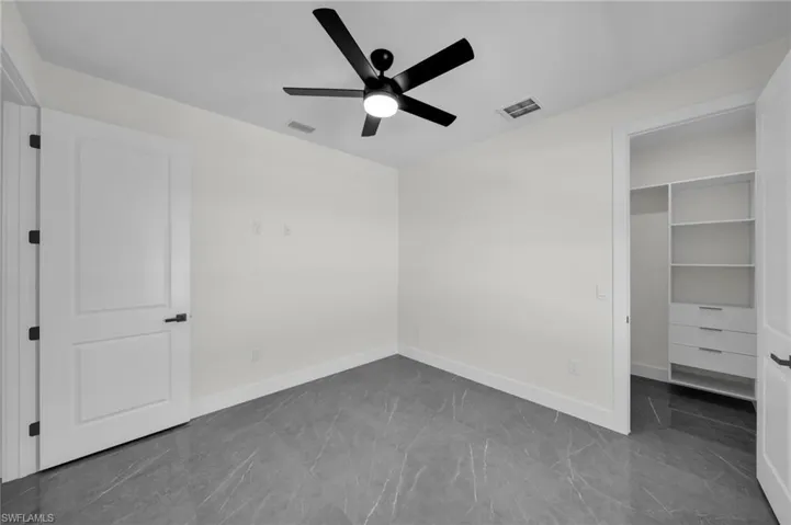Unfurnished bedroom with a spacious closet, visible vents, and baseboards