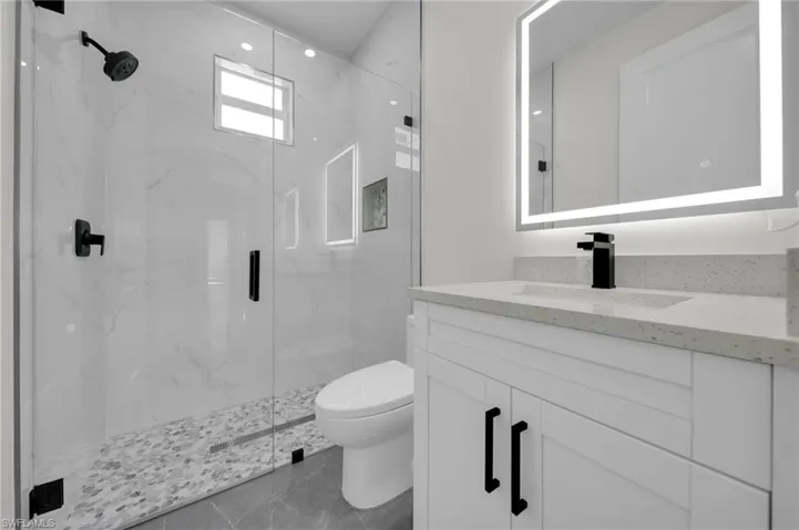 Bathroom featuring toilet, marble finish floor, a marble finish shower, and vanity
