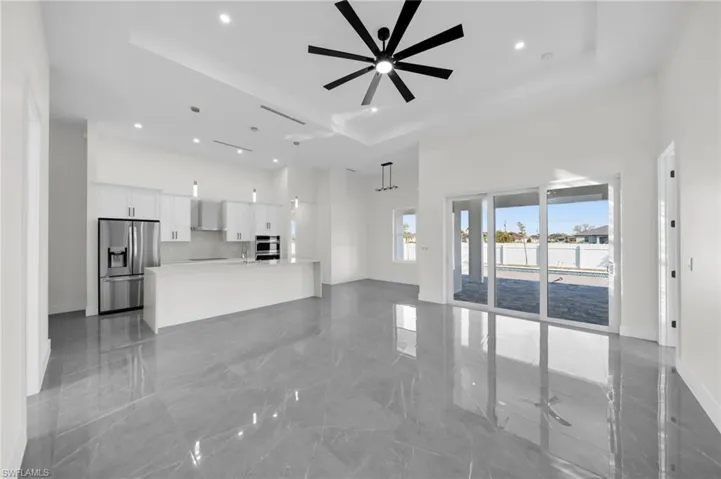 Unfurnished living room featuring a ceiling fan, a tray ceiling, marble finish floor, and a high ceiling
