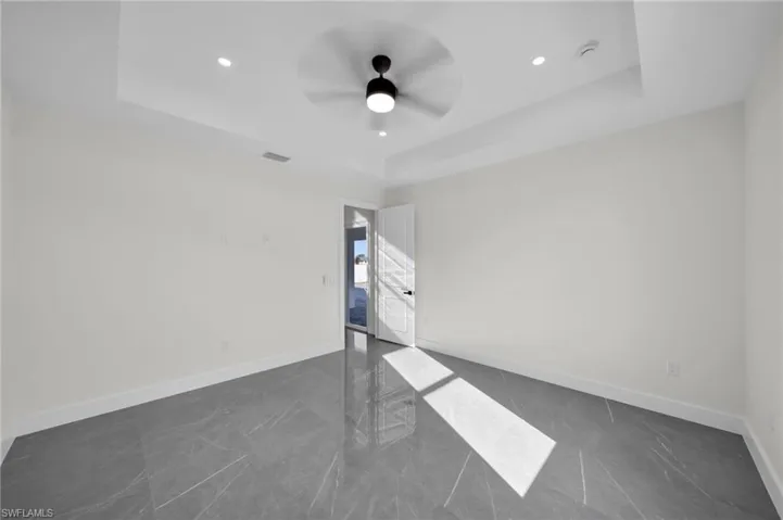 Unfurnished room featuring a ceiling fan, a tray ceiling, visible vents, and baseboards