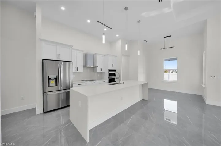 Kitchen with white cabinets, a towering ceiling, wall chimney exhaust hood, stainless steel appliances, and light countertops