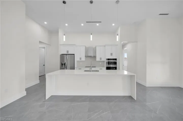 Kitchen with white cabinets, a large island, a high ceiling, stainless steel appliances, and wall chimney range hood