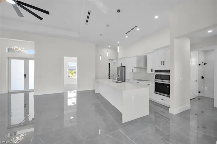 Kitchen with wall chimney range hood, a high ceiling, marble finish floor, and stainless steel appliances