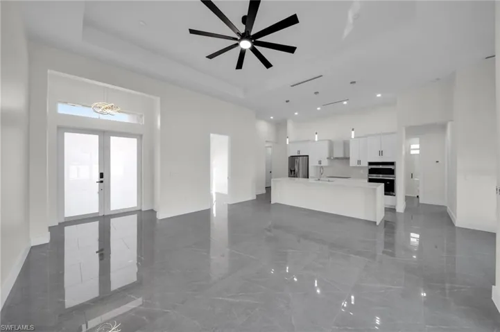 Unfurnished living room featuring a high ceiling, baseboards, a raised ceiling, and french doors