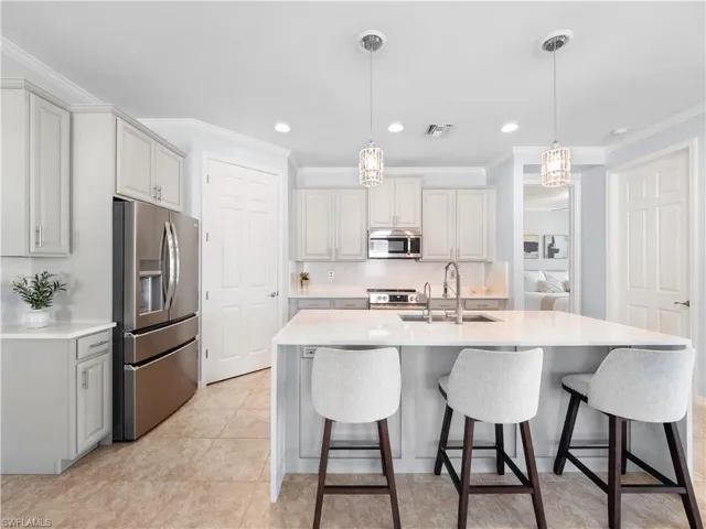 Kitchen featuring stainless steel appliances, pendant lighting, a kitchen breakfast bar, light stone counters, and crown molding