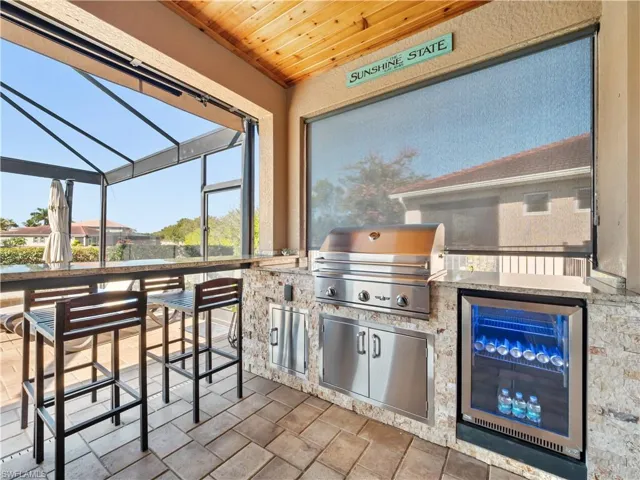 View of patio / terrace featuring beverage cooler, glass enclosure, a sunroom, and area for grilling