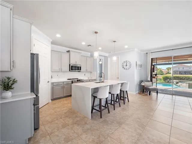 Kitchen with pendant lighting, a kitchen breakfast bar, light stone countertops, gray cabinetry, and a center island with sink