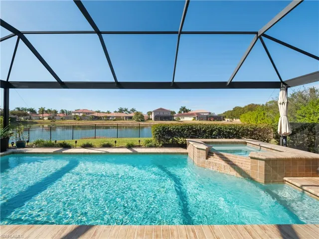 Combined pool / hot tub with glass enclosure, a fenced backyard, a water view, and a sunroom