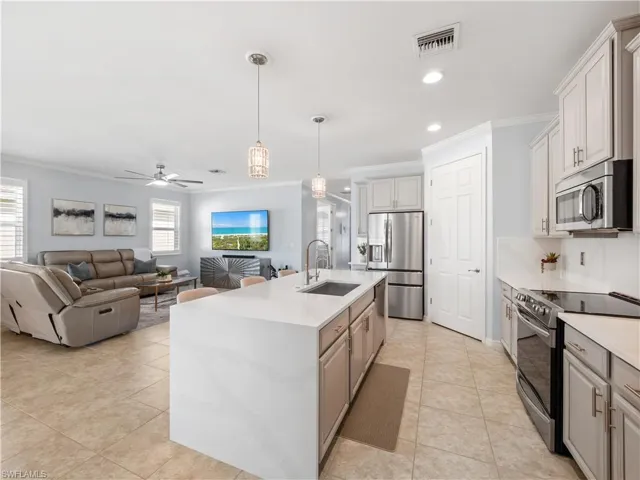 Dual tone kitchen with stainless steel appliances, hanging light fixtures, light tile patterned floors, ornamental molding, and a center island with sink