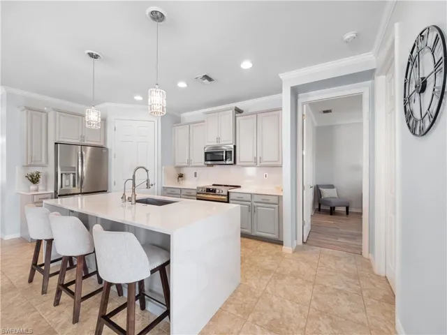 Kitchen with hanging light fixtures, backsplash, gray cabinets, stainless steel appliances, and ornamental molding