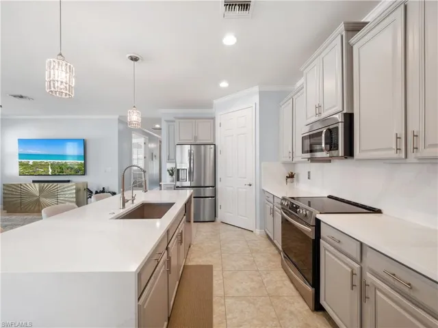 Kitchen with stainless steel appliances, decorative light fixtures, light stone countertops, ornamental molding, and open floor plan