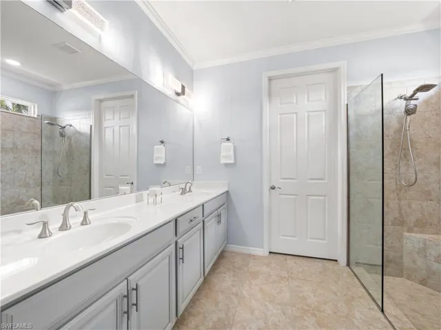 Bathroom featuring walk in shower, double vanity, ornamental molding, and light tile patterned flooring